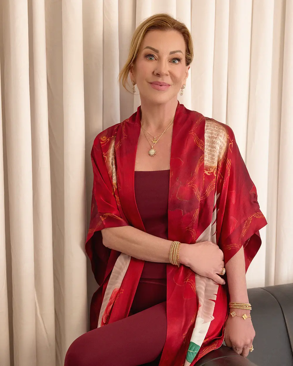 Stephanie in a red kimono robe, seated beside a draped curtain